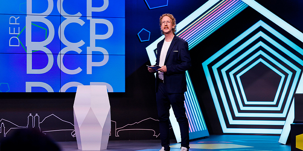 Moderator Uke Bosse moderiert auf der Bühne vor DCP Leinwand