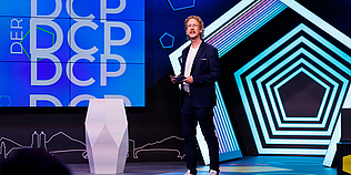 Moderator Uke Bosse moderiert auf der Bühne vor DCP Leinwand