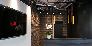Büro mit Empfangsbereich mit Hängeleuchten und Monitor mit Netflix-Logo