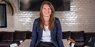 Bild von Lenka Kaciakova auf einem Tisch sitzend, Couch und Fernseher im Hintergrund