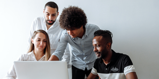 Gruppe von Mitarbeiter:innen die auf einen Laptop schauen