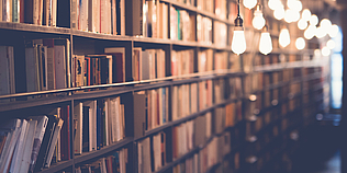 Langes Bücherregal und davor hängende Glühbirnen